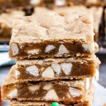 Stack of four pumpkin spice blondies with pumpkin candy and cinnamon stick and recipe title on top of image