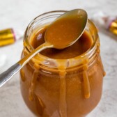 Three-ingredient caramel sauce in a small glass jar with a spoonful coming out