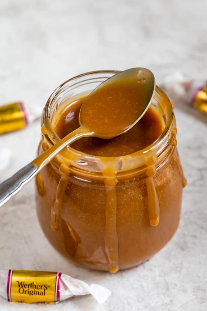 Three-ingredient caramel sauce in a small glass jar with a spoonful coming out