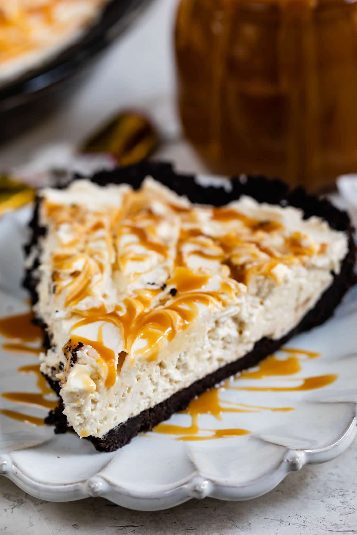 Close up shot of a slice of caramel cheesecake pie on a white scalloped plate