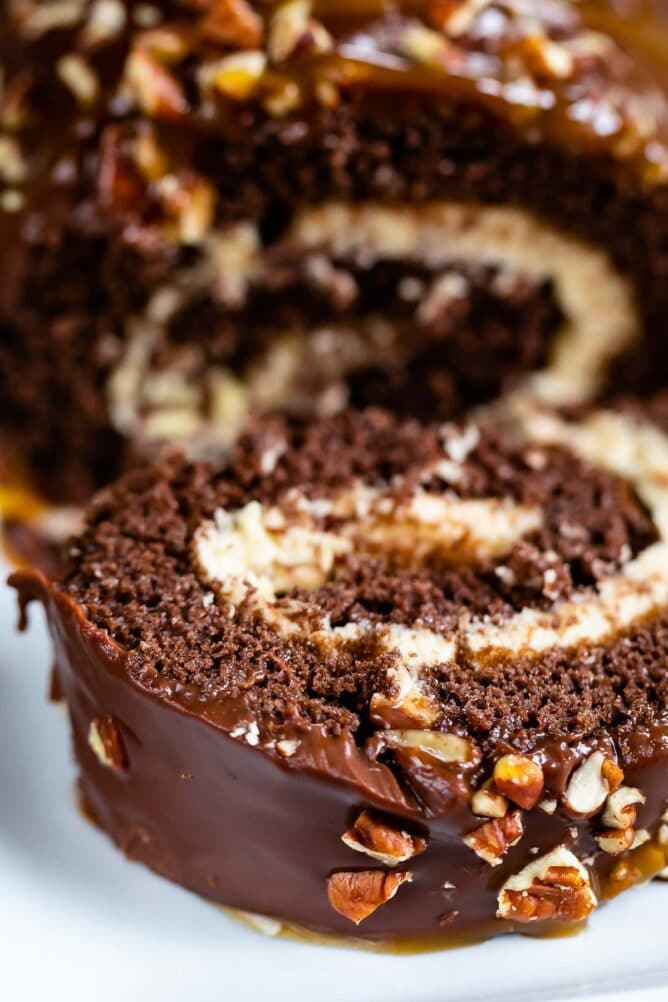 Close up shot of chocolate caramel turtle cake roll with one slice falling off