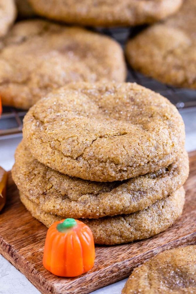 Three caramel stuffed pumpkin cookies with pumpkin candy next to them