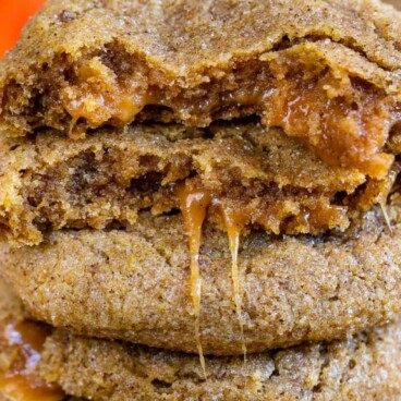 Caramel stuffed pumpkin cookies with top one cut in half to show inside caramel filling with recipe title on top of image