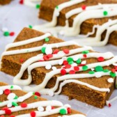Close up shot of gingerbread cookie bars decorated with white icing and red and green sprinkles with recipe title on top of photo