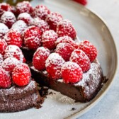 Close up shot of flourless chocolate cake topped with raspberries and powdered sugar