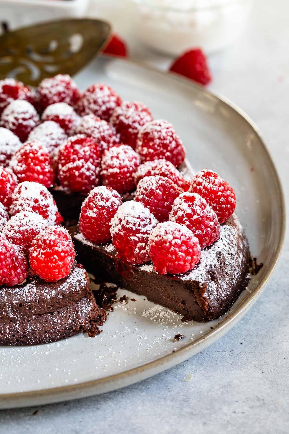 Close up shot of flourless chocolate cake topped with raspberries and powdered sugar