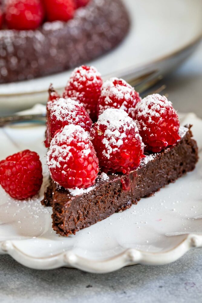 One slice of flourless chocolate cake topped with raspberries and powdered sugar