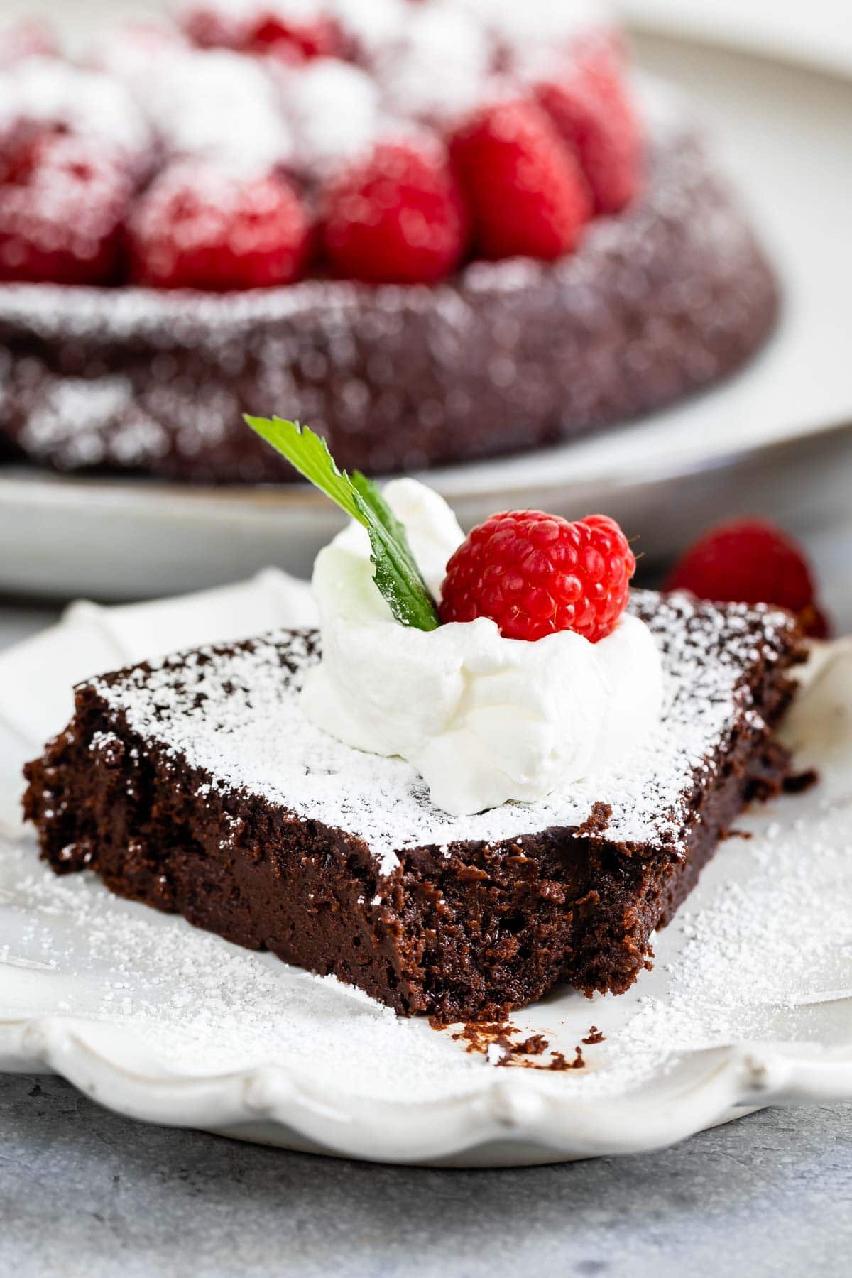 One slice of flourless chocolate cake topped with whipped cream, raspberry and mint