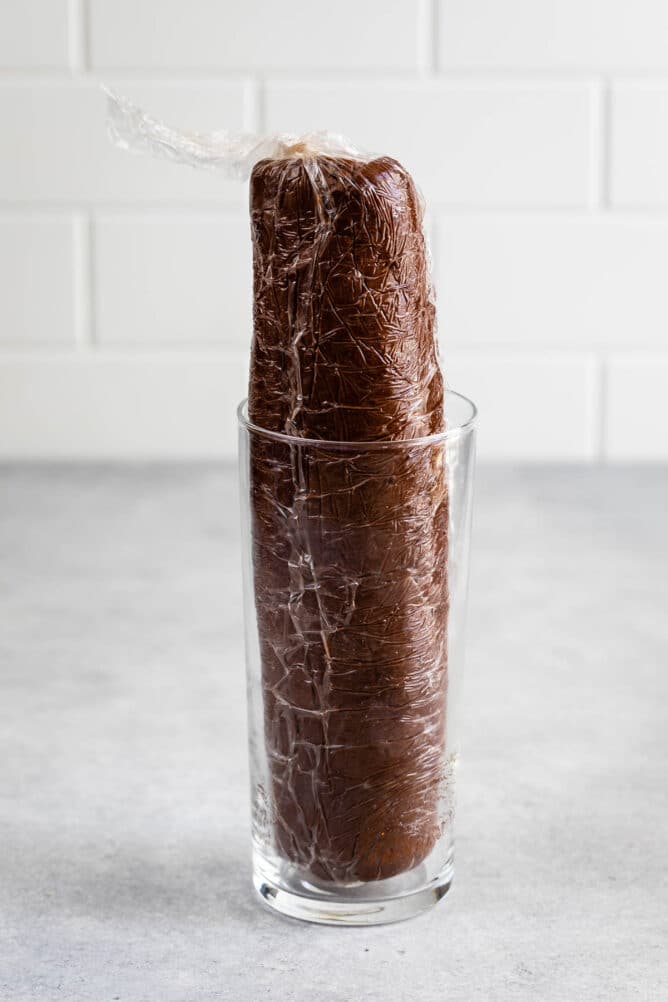 Chocolate shortbread cookie dough wrapped in plastic wrap and placed in a glass cup