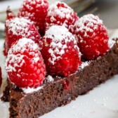One slice of flourless chocolate cake topped with raspberries and powdered sugar with recipe title on top of image
