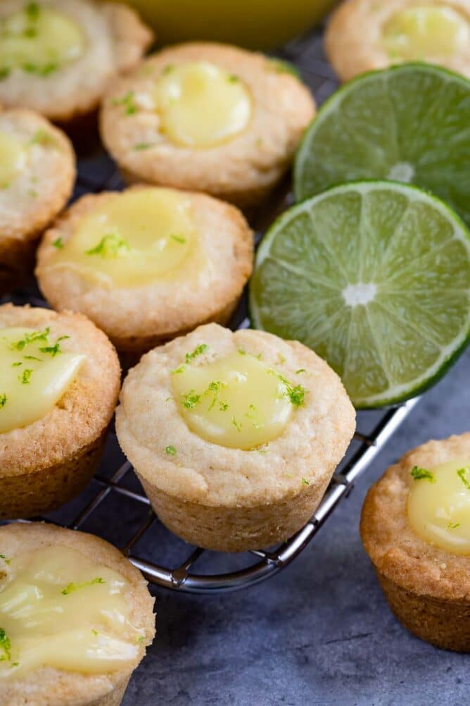 Mini lime tarts on a metal cooling rack next to limes