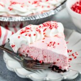 One slice of peppermint pie on a plate with fork and full pie in background