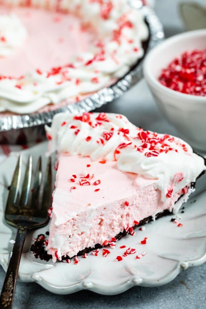 One slice of peppermint pie on a plate with fork and full pie in background