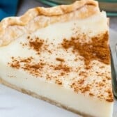 A slice of sugar cream pie dusted with cinnamon on a plate next to a fork.
