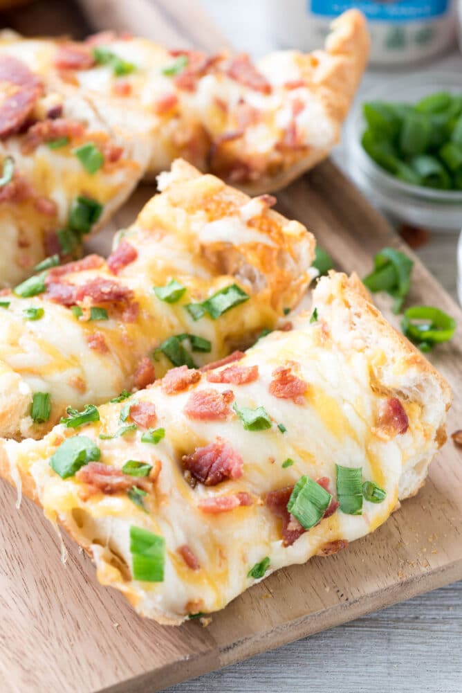 Slices of cheesy bacon ranch french bread pizza on wooden cutting board