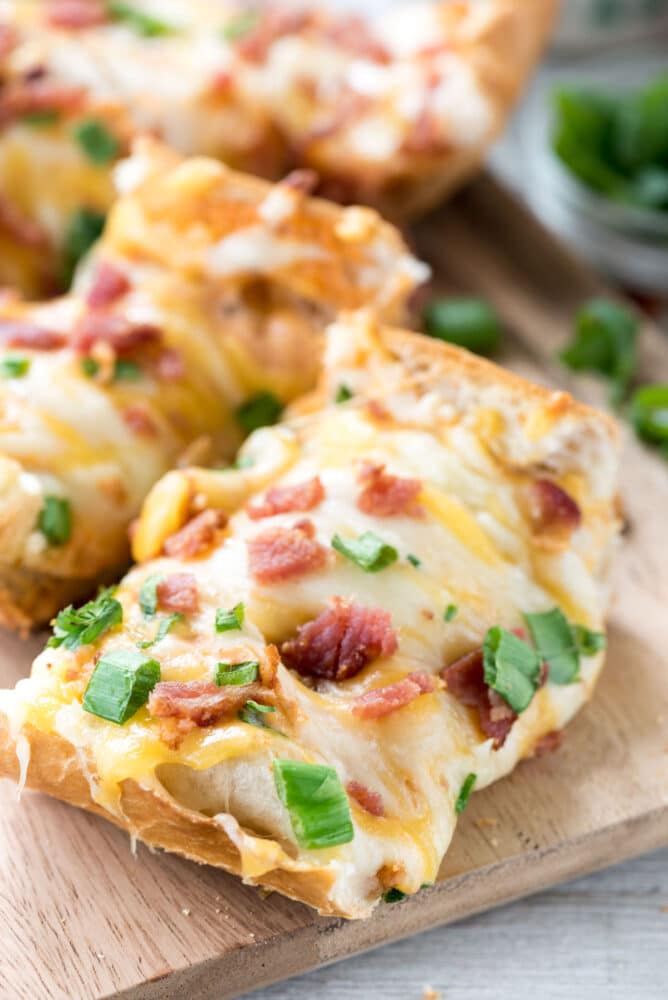 Slices of cheesy bacon ranch french bread pizza on wooden cutting board