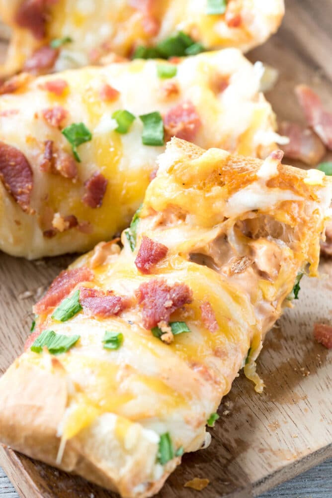Slices of cheesy bacon ranch french bread pizza on wooden cutting board