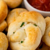 Close up shot of garlic knots next to dipping sauce and recipe title on top of image
