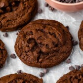 Double chocolate chip cookies on parchment paper with a bowl of chocolate chips