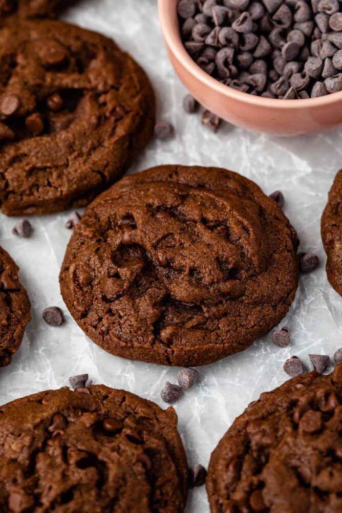 Double chocolate chip cookies on parchment paper with a bowl of chocolate chips