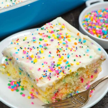 One square slice of homemade funfetti cake on plate surrounded by rainbow sprinkles