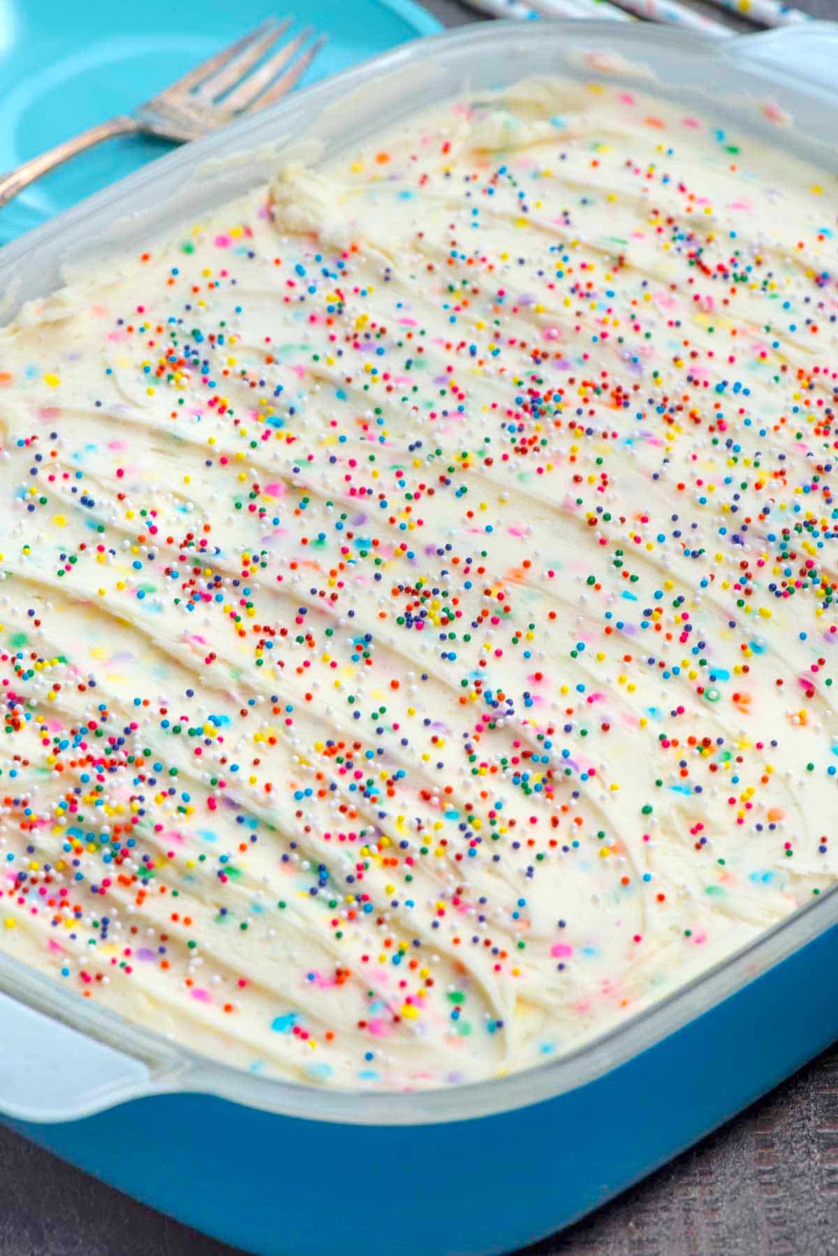 Homemade funfetti cake in a cake pan with vanilla frosting and rainbow sprinkles
