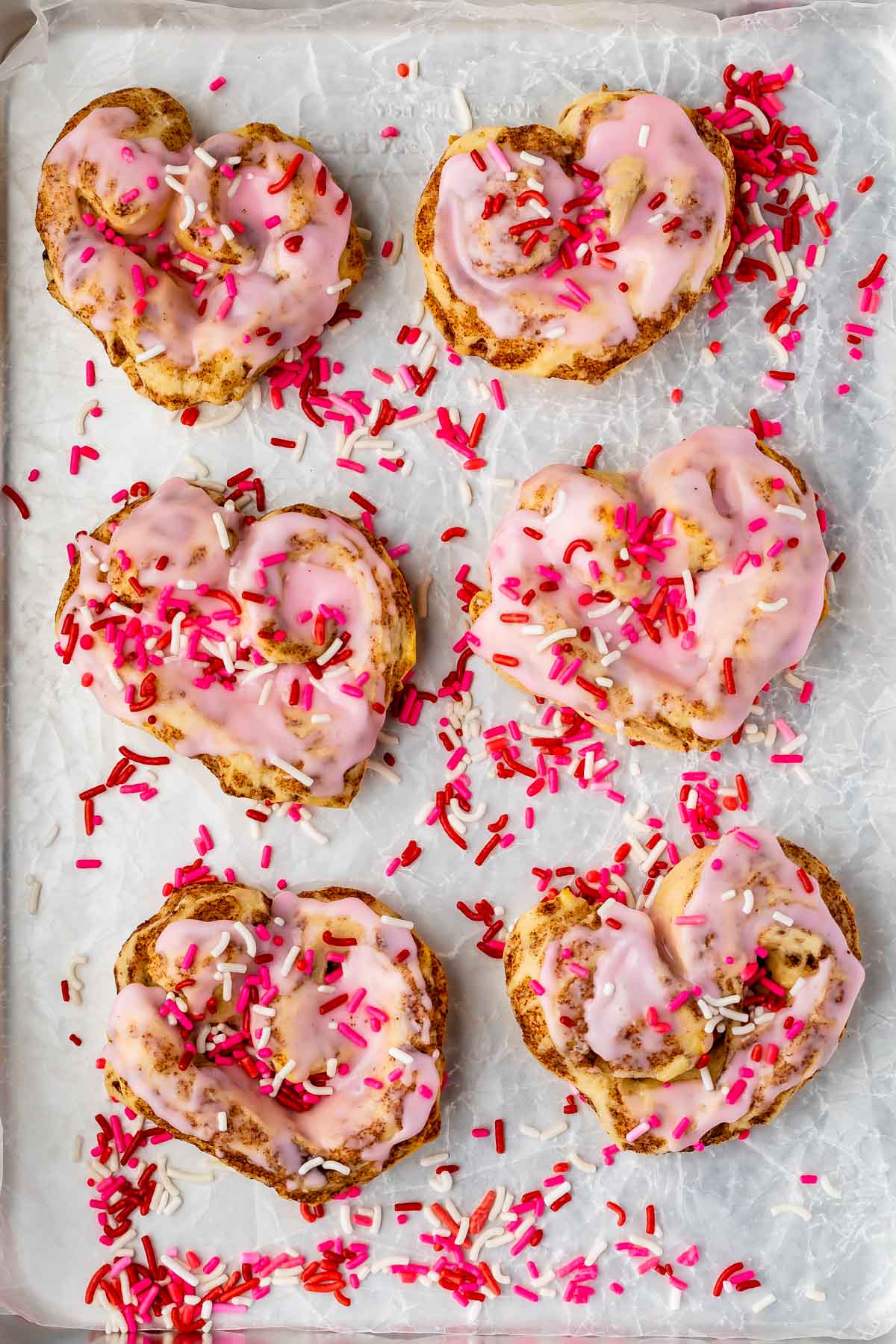 heart shaped cinnamon roll with pink icing and sprinkles on cookie sheet