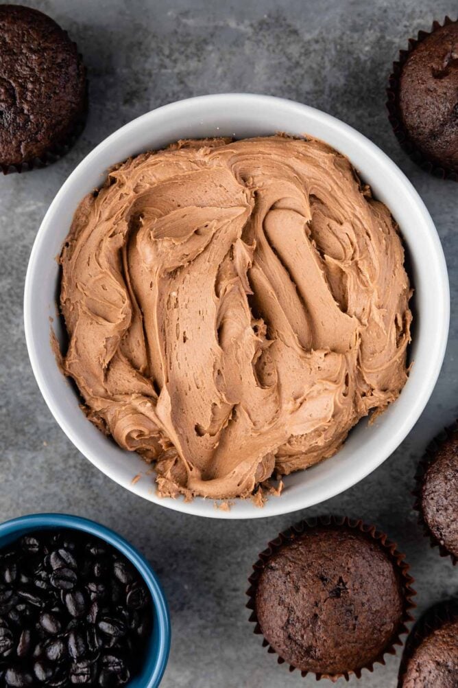 Overhead shot of mocha frosting in a ramekin surrounded by chocolate cupcakes