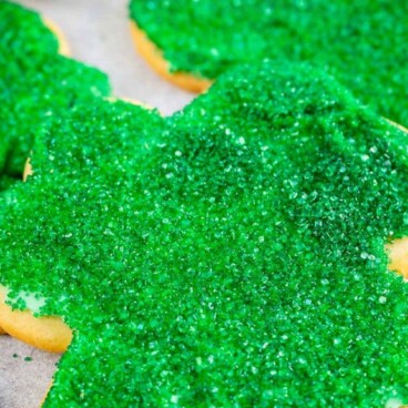 Close up shot of shamrock sugar cookies decorated with green sanding sugar and recipe title on top of image