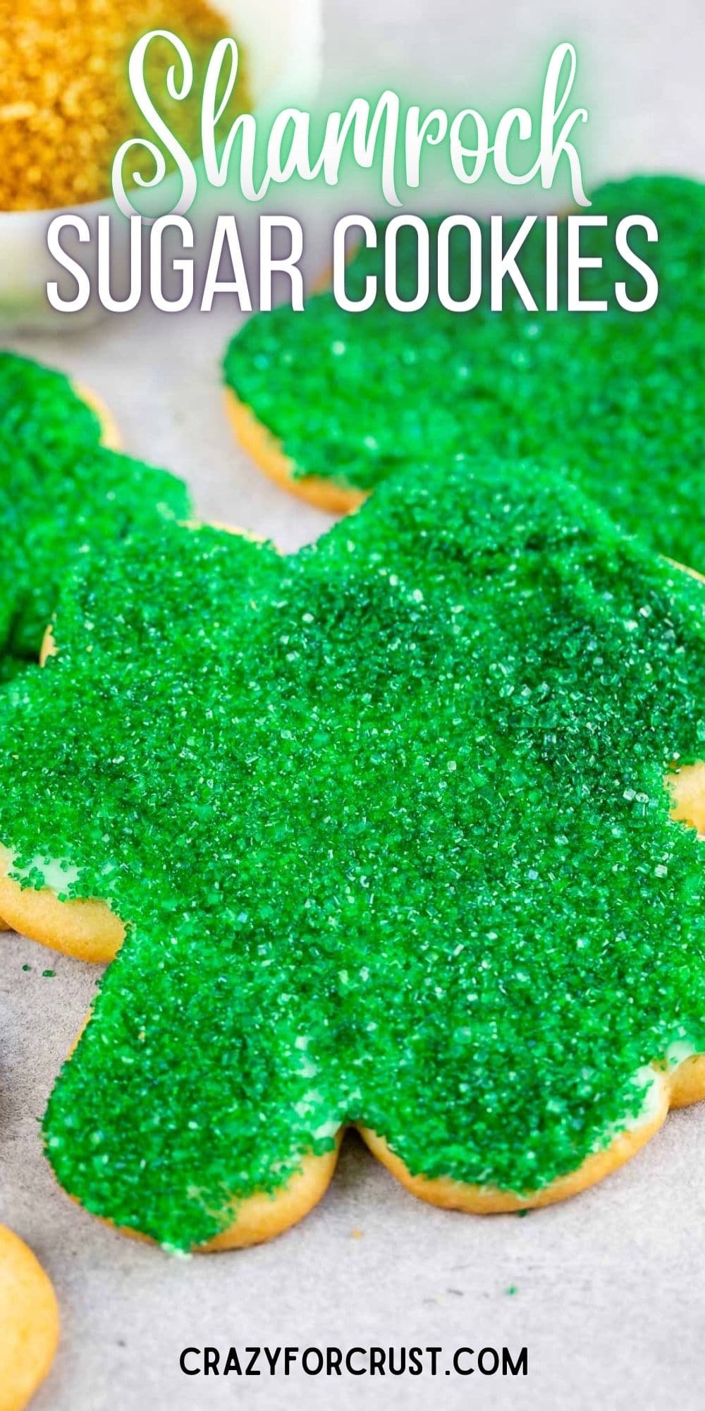 Close up shot of shamrock sugar cookies decorated with green sanding sugar and recipe title on top of image