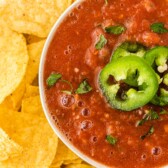 One bowl of easy salsa topped with sliced jalapenos surrounded by tortilla chips