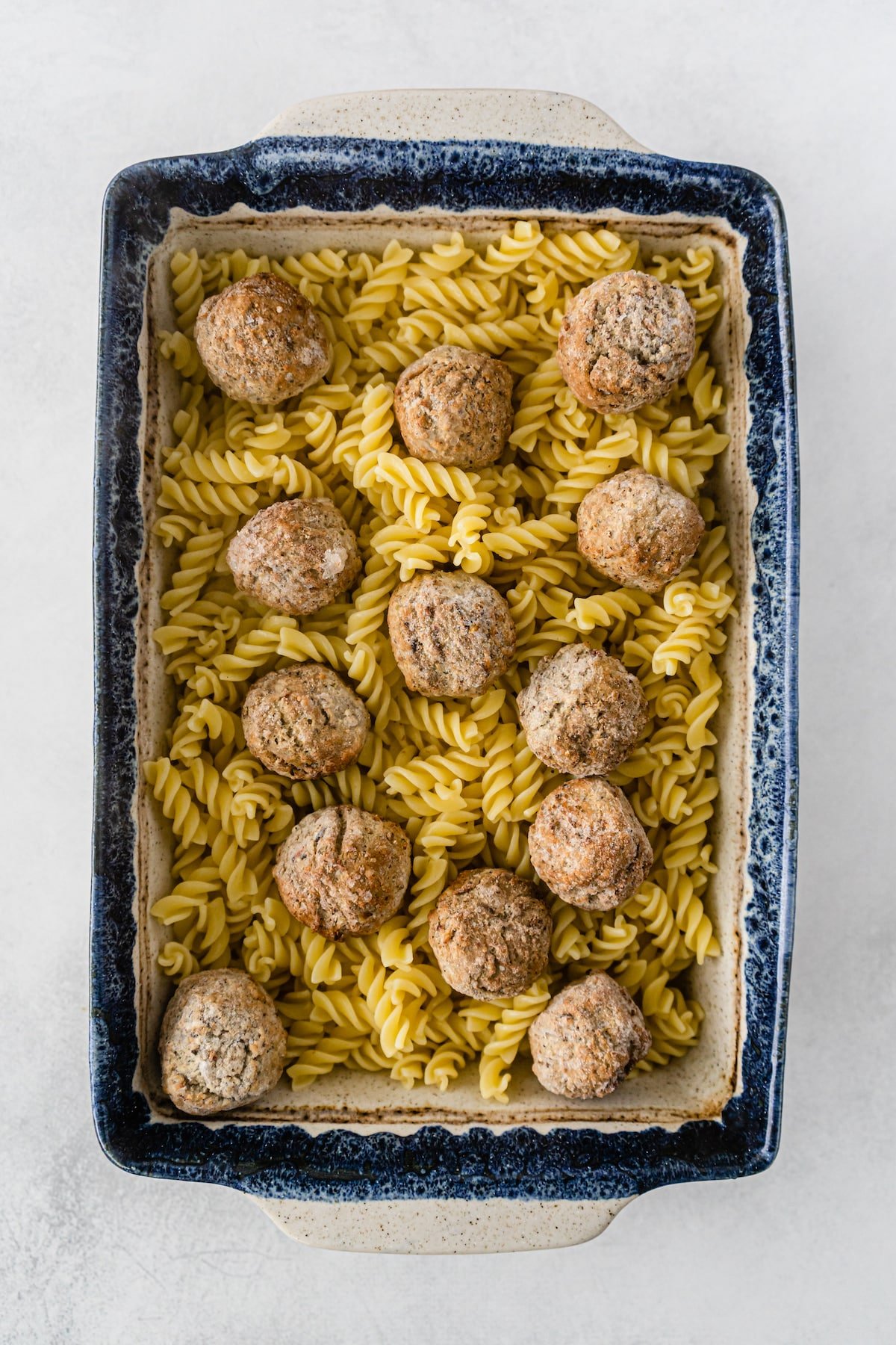 meatballs and cooked pasta in casserole dish.