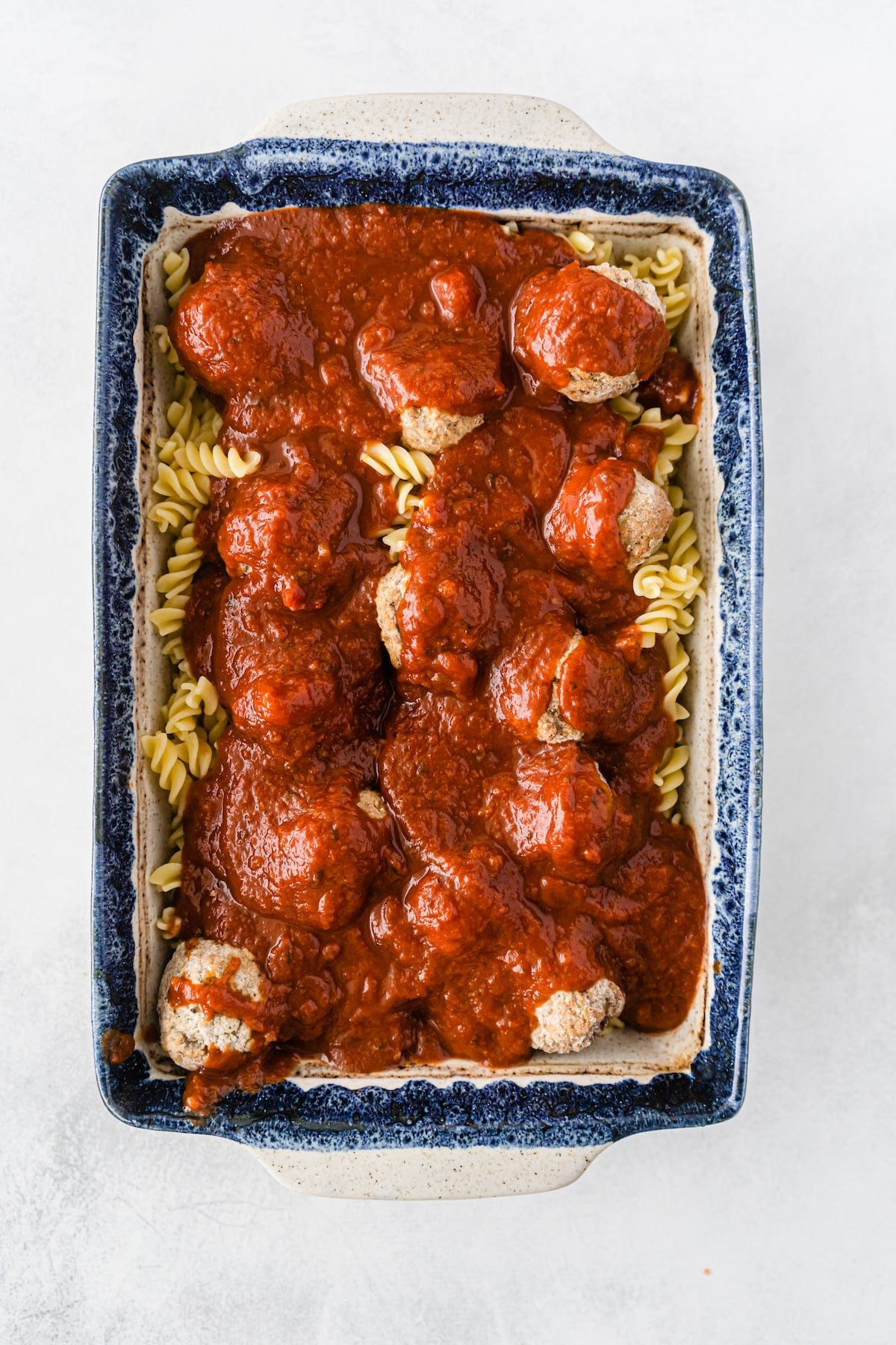 sauce over meatballs and cooked pasta in casserole dish.