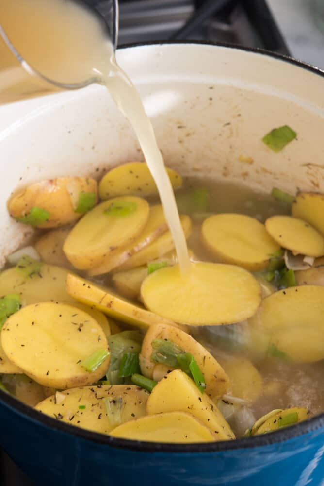 Broth being poured into the dutch oven over the potatoes and leeks