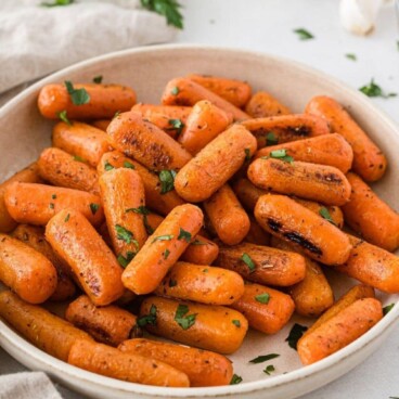 Roasted carrots in a white serving bowl with recipe title on top of image