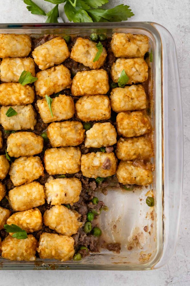 Overhead shot of hamburger tater tot casserole with corner piece missing from casserole dish