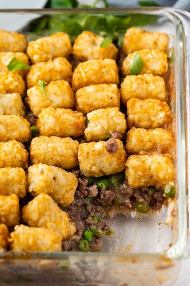 Overhead shot of hamburger tater tot casserole with corner piece missing from casserole dish
