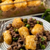 Hamburger tater tot casserole with gravy on a plate with full casserole dish in background