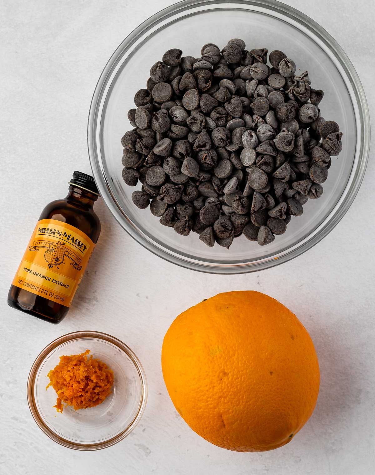 Overhead shot of chocolate chips, an orange, orange zest and orange extract