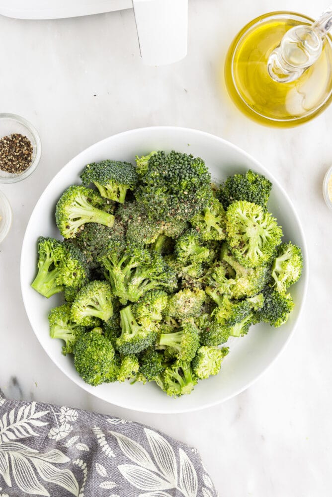 Overhead shot of broccoli in a bowl next to oil and salt and pepper
