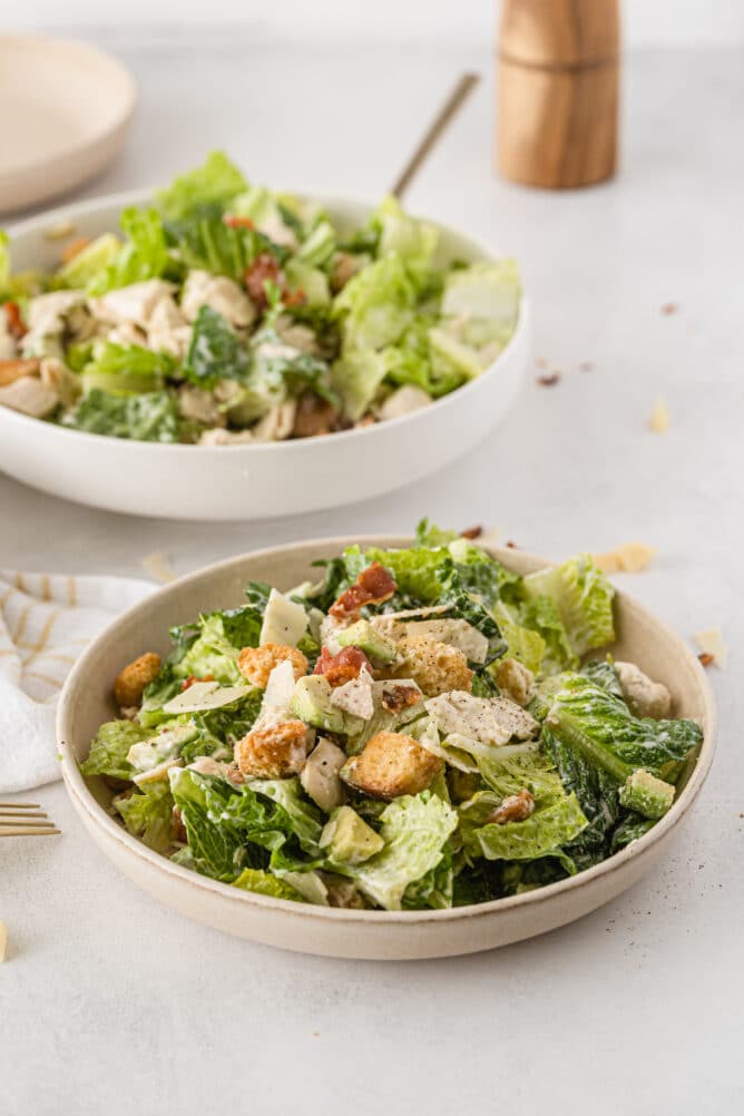 Two bowls of caesar salad with chicken and bacon