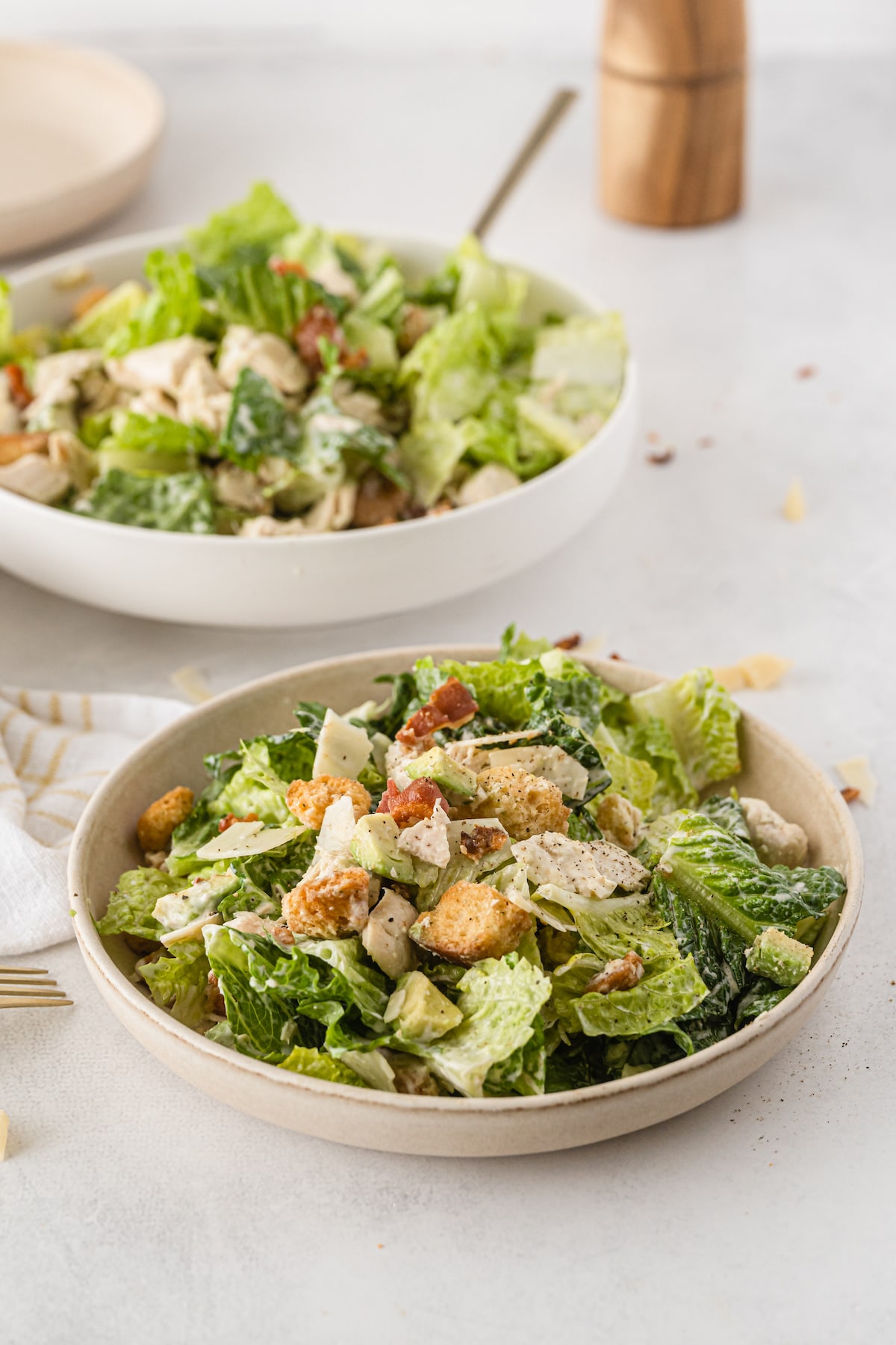 Two bowls of caesar salad with chicken and bacon