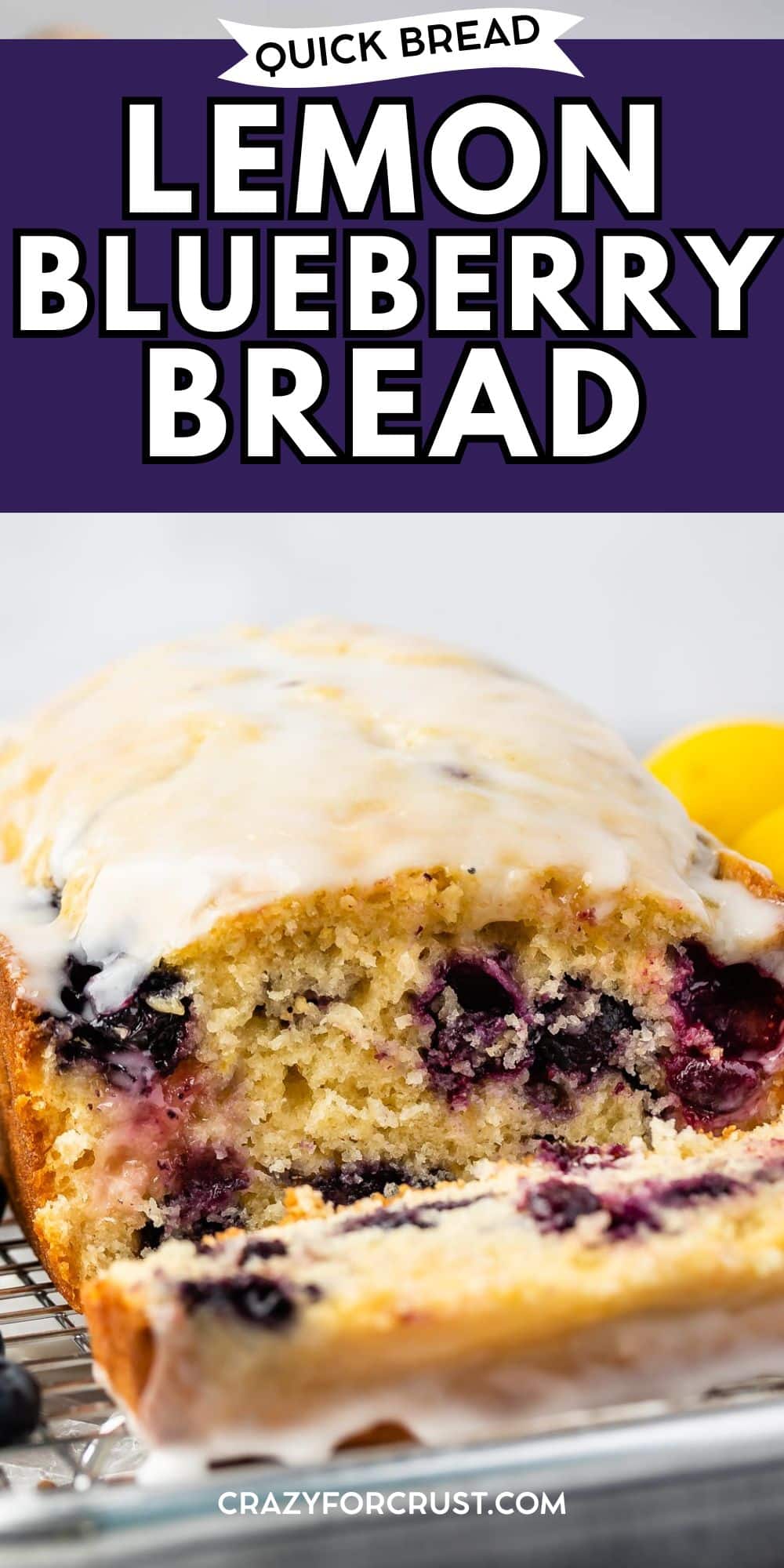 A loaf of lemon blueberry bread with white glaze sits on a cooling rack. A slice is cut, revealing juicy blueberries inside. Lemons in the background highlight this Quick Bread Lemon Blueberry Bread.