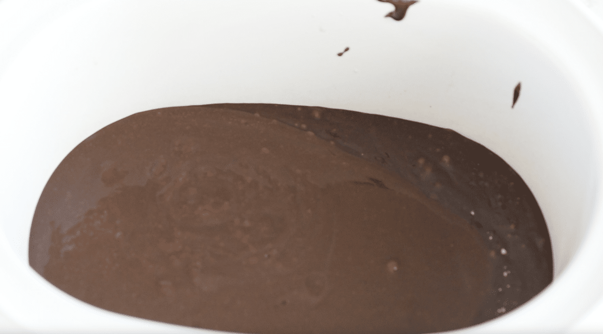 A white bowl filled with smooth, dark chocolate batter, with a few bubbles and streaks visible on the surface—just like what youd find in a decadent Slow Cooker Brownie Pudding.