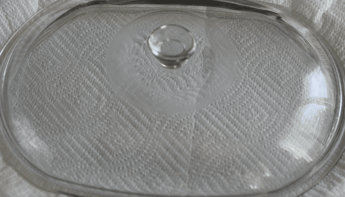 A clear glass casserole dish lid with a round handle sits on a textured white paper towel background, perfect for covering treats like Slow Cooker Brownie Pudding or crockpot lava cake.