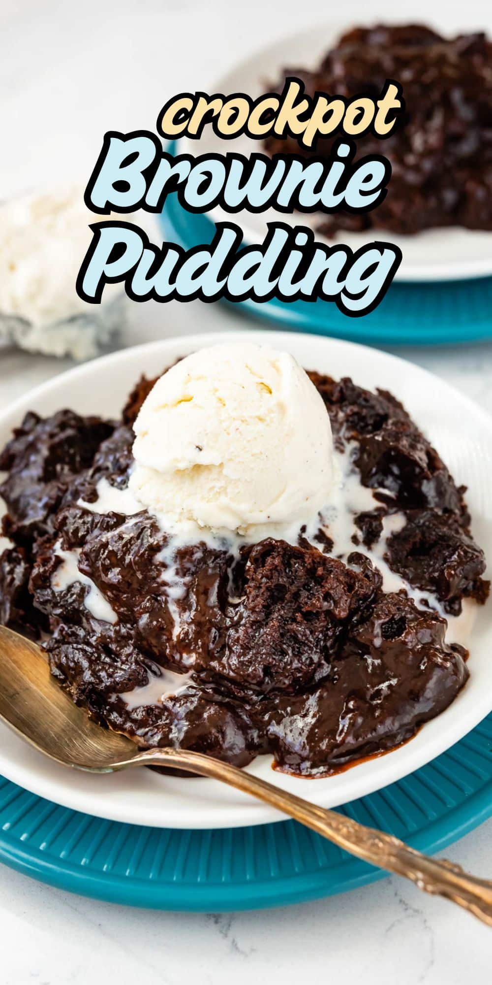 A plate of gooey Slow Cooker Brownie Pudding topped with vanilla ice cream, served with a gold spoon. Text on the image reads Crockpot Brownie Pudding. Another plate is visible in the background.