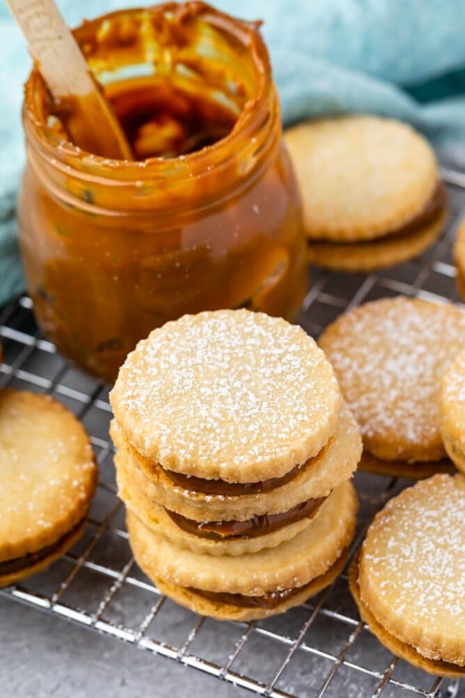 Overhead shot of dulce de leche cookies on a wire cooling rack next to a jar of dulce de leche