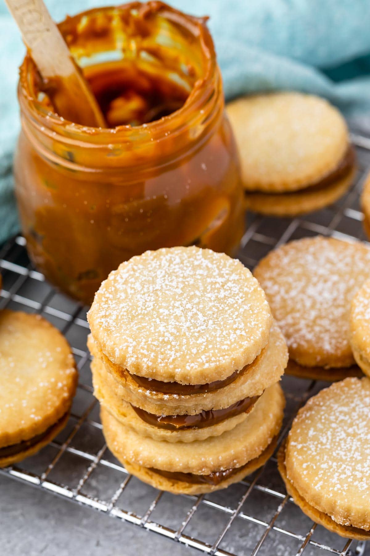 Overhead shot of dulce de leche cookies on a wire cooling rack next to a jar of dulce de leche