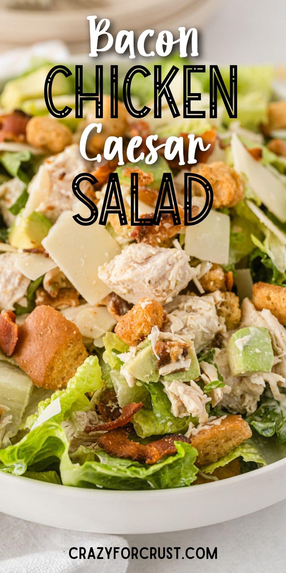 Close up shot of caesar salad with chicken and bacon in a bowl with recipe title on top of image