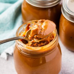 One spoon inside jar of dulce de leche with more jars in background